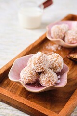 Handmade sweets, Laddu Indian sweet made from coconut, sugar and milk on a pink plate on a wooden tray. Vegan desserts, Vedic cuisine. Indian food