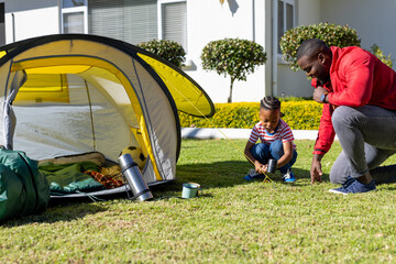 Happy african american son and father pitching tent together in sunny garden, copy space