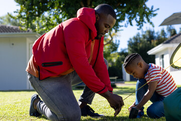 Happy african american son and father pitching tent together in sunny garden