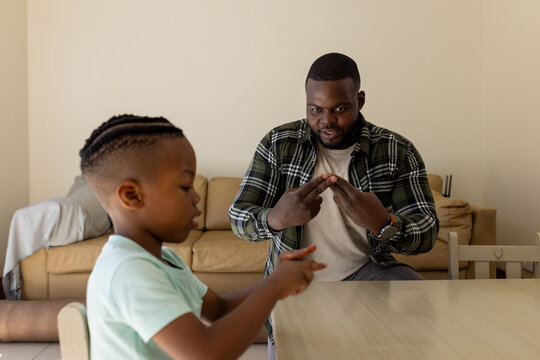 Happy african american father and son practicing sign language together at home