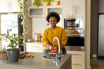 Happy plus size african american woman rinsing vegetables in kitchen