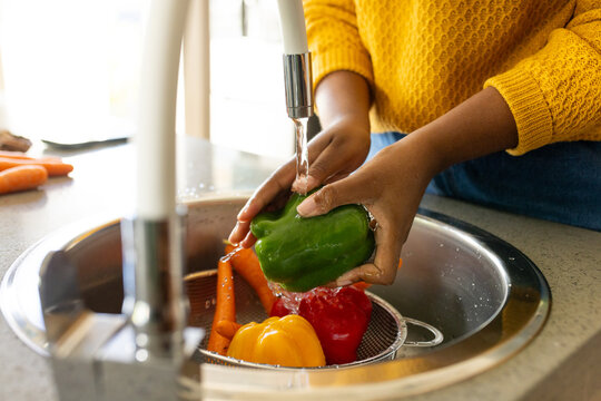 Hands of plus size african american woman rinsing vegetables in kitchen