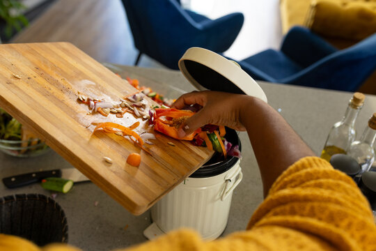 Hand of plus size african american woman in apron composting vegetable waste in kitchen