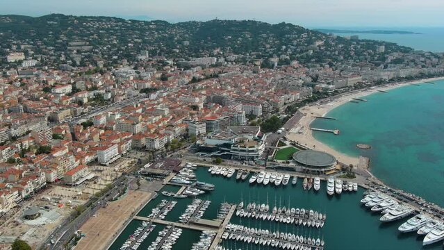 Aerial helicopter view of IGY Vieux-Port de Cannes marina, picturesque port for boats - yachts with panoramic city skyline of Croisette Beach and Palais des Festivals, hosting Cannes Film Festival 4K