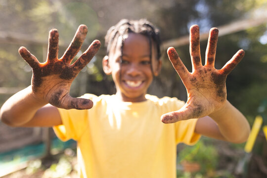 Portrait of happy african american boy showing his hands covered in ground in garden