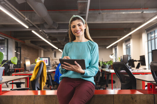 Portrait of biracial woman smiling while using a digital tablet at office