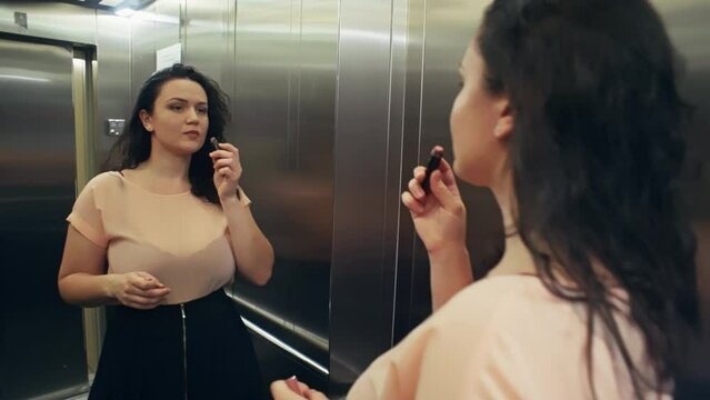 A Caucasian woman enters the elevator and paints her lips before a party. The girl is in a hurry to go on a date. High quality 4k footage