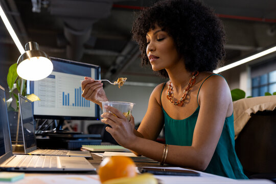African american woman having a snack sitting on her desk at office