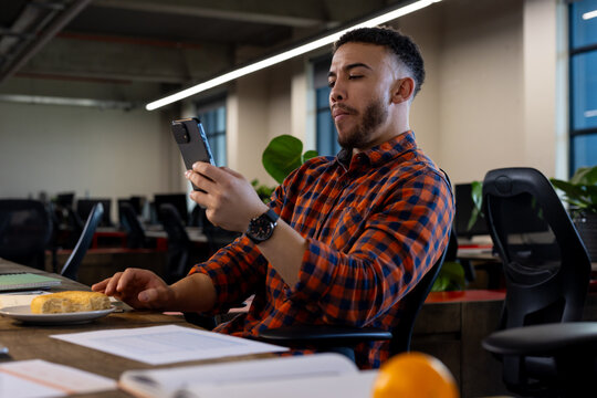 Biracial man using smartphone while having a snack at office