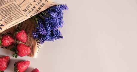 Red fresh strawberry and purple muscari flower with an vintage newspaper on white background, with copy space for text