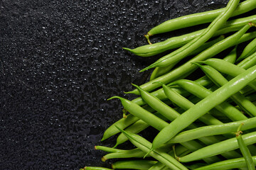 A group of green pods of raw, uncooked, asparagus beans on a black stone background. Top view. Copy space.