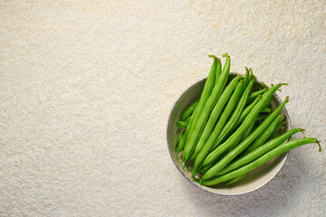 A bowl with pods of raw asparagus beans and a knife on a light marble background with copy space. Top view.
