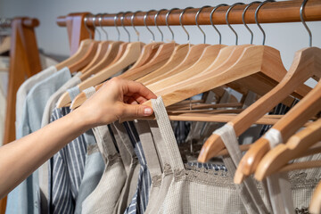 Naklejka premium Choice of clothes made from ecological natural fabrics. Closeup of hand touch dress put up for sale on wooden hangers in store. Varied reuse clothing hangs neatly on eco-friendly second hand rail.