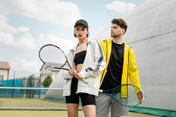 fashionable sportswear, man and woman holding tennis rackets on court,  sport and style