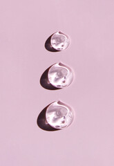 round drops of transparent gel serum on pink background - obrazy, fototapety, plakaty