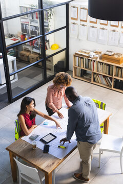 Happy diverse colleagues discussing work with tablet over project of building in office