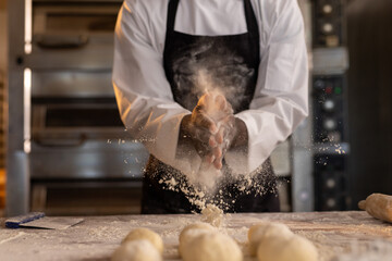African american male baker in bakery kitchen clapping hands with flour