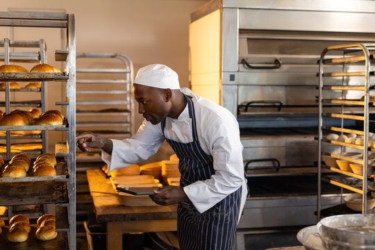 Focused african american male baker in bakery kitchen counting rolls