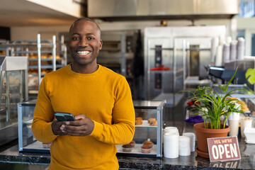 Portrait of happy african american male bakery worker using smartphone