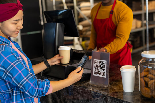 Happy diverse male bakery worker and customer scanning qr code with smartphone