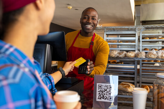 Happy Diverse Male Bakery Worker And Customer Paying With Credit Card