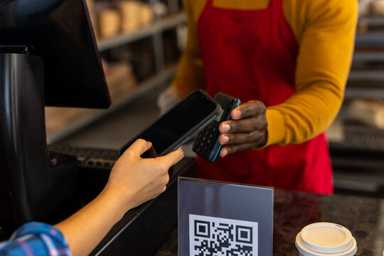 Diverse male bakery worker and customer paying with smartphone with copy space