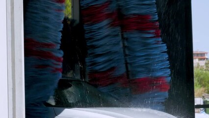brushes washing a white car in a car wash service