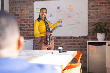 African american casual businesswoman making presentation on whiteboard using tablet in meeting room