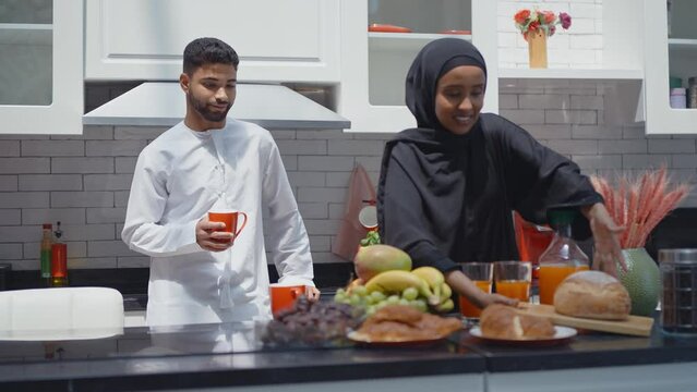 Happy couple wearing traditional outfits from the emirates spending  time in the kitchen of their beautiful modern apartment in Dubai