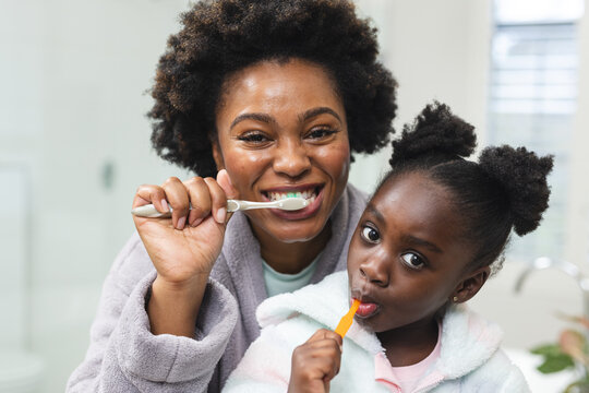 Happy african american mother and daughter washing teeth in bathroom at home