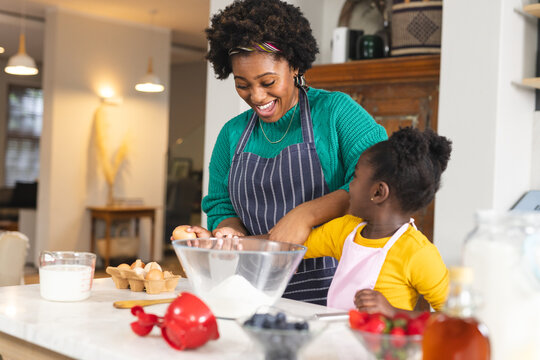 Happy african american mother and daughter baking pancakes in kitchen at home