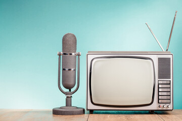 Vintage old television and microphone on wooden table front gradient mint blue wall background. Retro style filtered photo