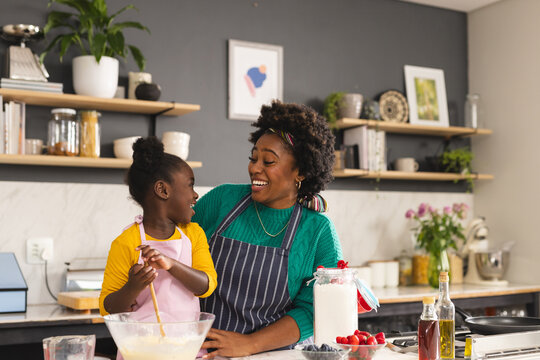 Happy african american mother and daughter baking pancakes in kitchen at home