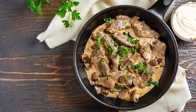 delicious beef stroganoff - veal strips stewed with porcini in sour cream sauce sprinkled with finely chopped parsley on skillet, authentic recipe, view from above