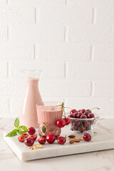 Freshly made homemade cherry smoothie in a bottle and a large glass on a stone board podium with berries and mint leaves. Detox.