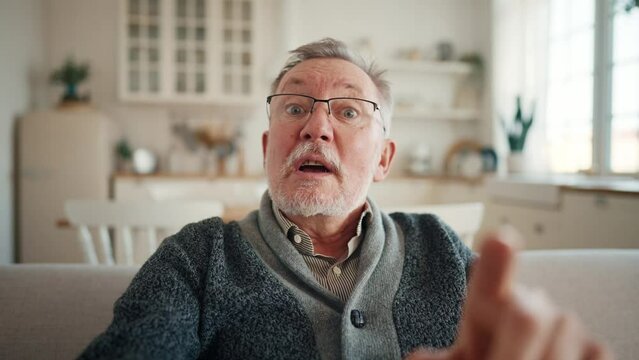 Grumpy grouchy senior man makes claims, swears, chastises, sarcastically jokes talking online on video call looking at camera. Old male in glasses discuss, has interesting conversation, grumbling.