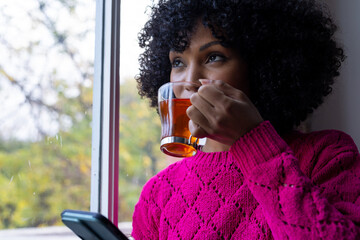 Biracial woman drinking tea and using smartphone at home