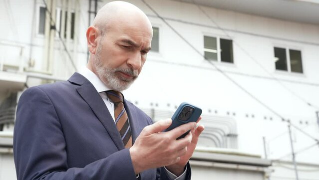 A Caucasian businessman using a smart phone in a local city.