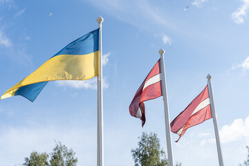 Ukrainian and Latvian flags together on flag poles waving in wind