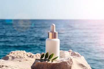 Cosmetic serum bottle on stone on the background blue sea in sunlight, closeup