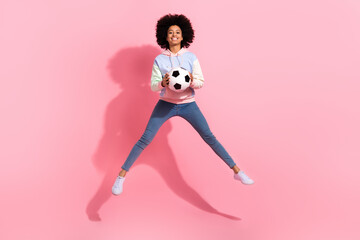 Fototapeta na wymiar Full length photo of excited pretty little child dressed hoodie jumping high catching football ball isolated pink color background