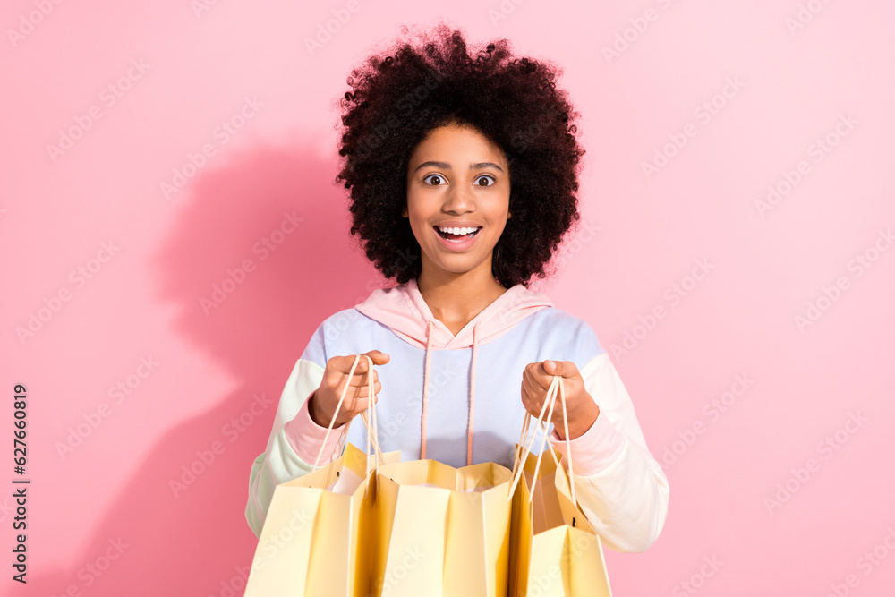 Sticker Photo of pretty surprised little child dressed hoodie open mouth open shopping packages isolated pink color background