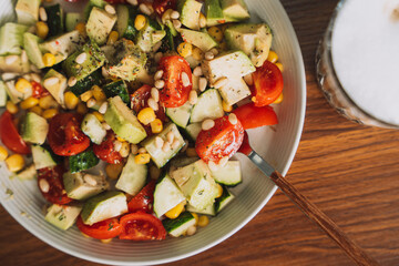 Vegetable salad with nuts on a white plate with a cup of coffee.