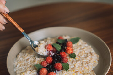 Oatmeal with raspberries and currants in a white cup with a spoon.