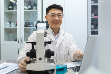 Portrait of young male Asian student, intern studying and working in laboratory with microscope and...