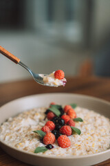 Oatmeal with raspberries and currants in a white cup with a spoon.