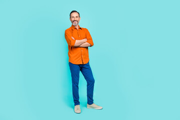 Full length photo of charming cute guy wear orange shirt arms folded empty space isolated teal color background