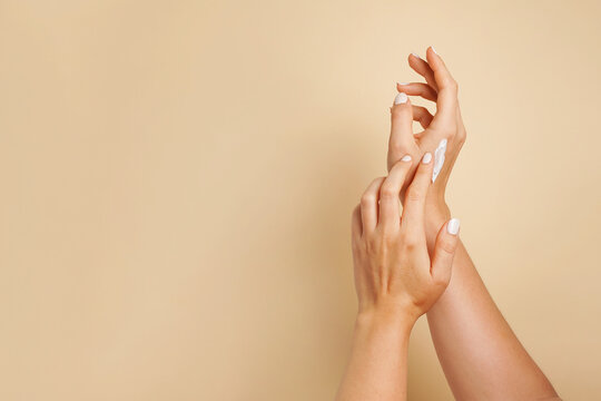 Beautiful young woman hands with cosmetic cream. Woman applies cream on her hands on beige background, copy space