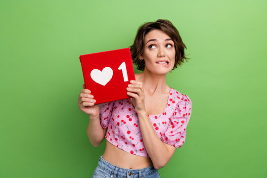 Portrait of thoughtful girl wear stylish blouse look empty space biting lips hold social media like isolated on green color background - Powered by Adobe