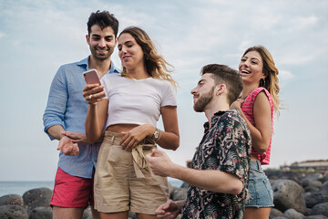 Two Young Couples Having Fun at Seaside with Smartphone - Young Caucasian friends enjoying their vacation at a rocky seaside, laughing and sharing content on a smartphone